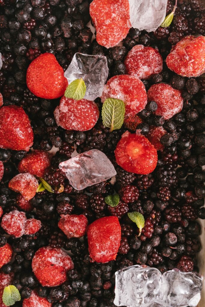 A vibrant vertical shot of mixed berries with ice cubes and mint leaves, perfect for refreshing summer recipes.