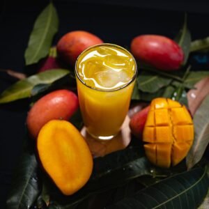 Close-up of a refreshing mango juice with whole and sliced mangoes on tropical leaves.
