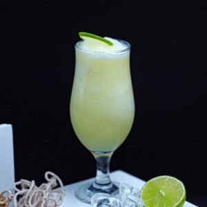 A refreshing lime smoothie in a glass with a lime garnish and ice cubes on the side.