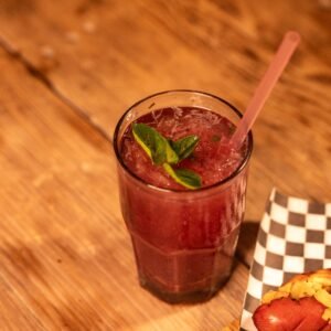 Cold berry cocktail with mint leaves and a hot dog on a wooden table in casual dining setting.