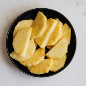 Top view of black ceramic bowl with slices of fresh sweet yellow pineapple placed on marble surface